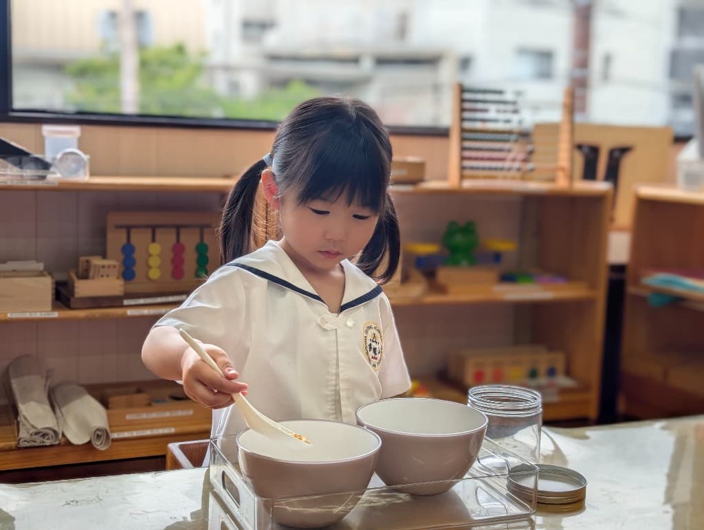 A student practising Montessori practical life skills by spooning grains between bowls